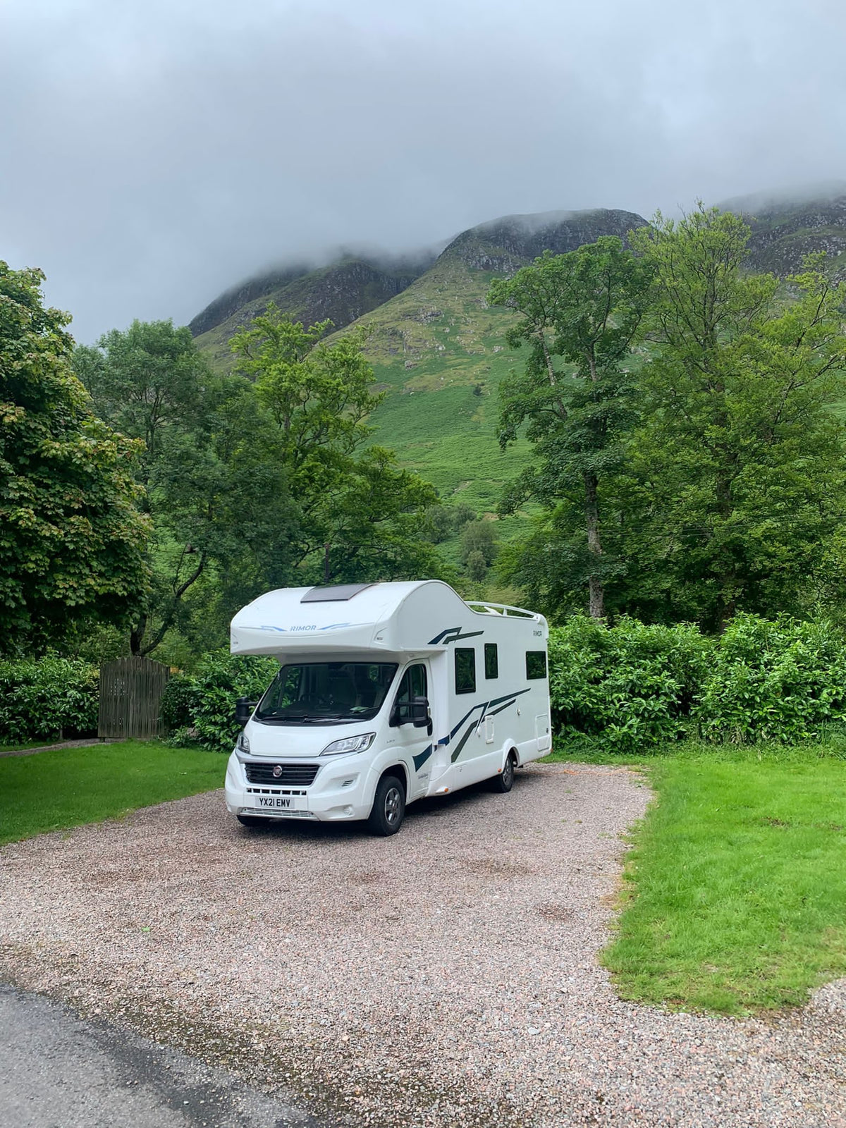 A white Rimor motorhome on a gravel pitch below misty hills in the Scottish Highlands